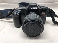 Front view of Canon EOS Rebel camera with attached Canon Zoom Lens EF 35-80mm 1:4-5.6 and lens cap on, showing camera body, grip, and strap attachments.