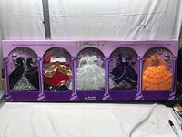 Long view of boxed set showing five different classic styled doll outfits, each visible in a purple box with plastic window.
