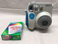 Front view of Fujifilm Instax Mini 7 camera with blue grip beside a 10-exposure box of Fujifilm Instax Mini instant film.