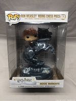 Front view of the boxed Funko Pop figure showing Ron Weasley riding a black chess piece with the Harry Potter and Movie Moments branding.