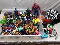 Overview of the lot showing multiple action figures and character toys in a large clear bin plus additional toys on the table.