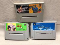 Three Super Famicom game cartridges: Dragon Ball Z with green label, Pilotwings with blue sky label, and Exhaust Heat with black label featuring a blue character.