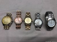 All five wrist watches arranged in a row showing different metal finishes and dial designs.