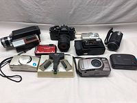Lot of old and modern cameras including digital compacts, SLR film camera, and battery charger accessory