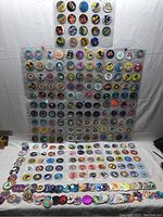 Wide view of about 112 collectible pog discs arranged on a white surface and pinned sheet. Various colorful and graphic designs visible.