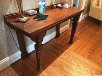 Full view of antique wood table showing carved straight legs with fluting and decorative brackets under tabletop corners, surface with wear and finish nicks.