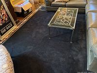 Full view of navy blue area rug in living room setting with glass coffee table and black leather couches.