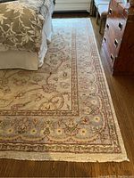 Corner view of rug under bed showing border pattern and fringe