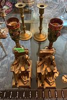 Photo showing two ornate colorful candle stands and two slender brass candle stands with measuring tape