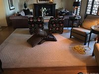 Living room with the large beige carpet covering most of the floor under floral print chairs, a striped sofa, and cushions on top of the carpet.