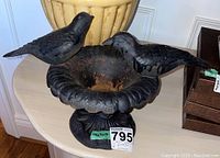 Front and angled view of black cast iron urn with two birds perched on the rim, showing surface rust inside, placed on a table.