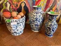 Three ceramic items: a round planter with blue and white detailed designs, filled with faux fruit in colors including orange and peach, accompanied by two blue and white patterned vases of different sizes.
