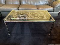 Full view of the rectangular coffee table showing the brushed metal base and clear glass top with visible scratches and chip on one corner.