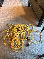 Yellow extension cord coiled on carpet beside furniture, showing full length and connectors.
