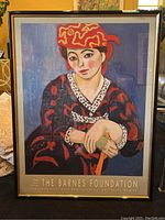 Full view of framed Henri Matisse art poster showing seated woman in red hat and patterned clothing with black and gold plastic frame