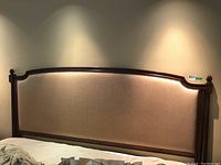 Front view of full upholstered headboard in beige fabric and dark wood frame