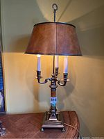 Full view of lamp showing metal base, composite section, triple candle-style bulbs and brown lampshade