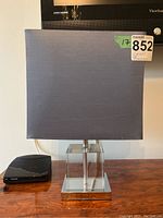 Front view of the table lamp showing gray fabric shade atop clear acrylic section on metal base.