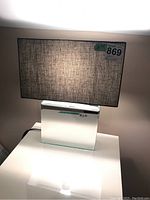 Table lamp with light fabric shade on mirrored base, illuminated to show light diffusion through shade