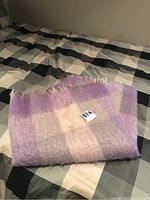 Folded purple and pink checkered mohair throw blanket laid on a bed showing a stain on the surface