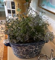 Front side view of blue and white ceramic planter with faux white flowering greenery inside, showing intricate blue motifs and side handles.