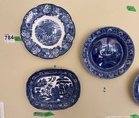 Four blueware decorative plates mounted on a wall, showing blue and white pastoral scenes including cottages and trees, floral patterned borders, and one rectangular plate with a scenic design.