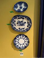 Three blueware decorative plates arranged vertically on a yellow wall, showing size variations and blue intricate patterns.