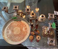 Full view of silver plate tableware including tray, candleholders, shakers, and mills on glass table showing condition and details.