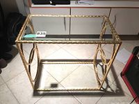 Front and top view of the wrought iron table with metallic finish and glass top showing overall design and size in tiled floor setting.