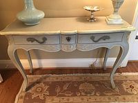 Frontal view of the wood console/vanity table showing painted finish, drawer details, and carved legs.