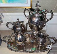 Full view of five-piece tea service including teapot, tapped urn, cream jug, and sugar bowl arranged on a silver tray (tray not included in lot).