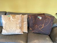 Four large throw cushions displayed on a leather couch: two brocade style cushions on the left and two horse-themed cushions on the right.