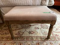 Front view of rectangular upholstered bench with beige fabric and wooden legs showing detailed wood base.