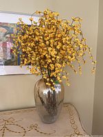 Full view of vase with faux yellow forsythia branches placed inside on a table.