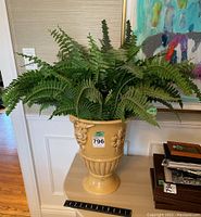 Front view of the large ceramic vase with faux fern plant on top of a table, showing its size relative to furniture.