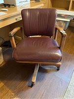 Front view of a vintage wooden office chair with maroon vinyl upholstery on seat and back showing wear.