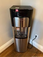 Full front view of the Viva water cooler/heater showing the black top section, stainless steel front panel, dispensing area, and removable drip tray.