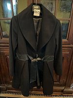 Full front view of black wool coat with leather waistband belt.