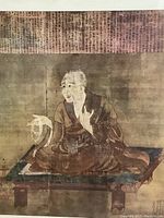 Close up of one framed Buddhist print showing seated monk figure on platform with prayer beads and background script