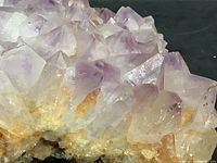 Close-up photo showing pointed purple amethyst crystals with white and orange mineral base
