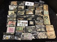 Overview of three USPS stamp sets and multiple zip bags containing assorted foreign coins and paper money