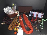 Wide view of assorted necklaces, earrings, brooch, clutch, and small box with baggies