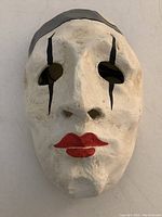 Front view of handcrafted Pierrot mask showing white surface, black tear lines, and red lips.