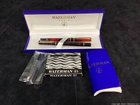 Opened presentation box showing two pens, sealed cartridge packet, loose cartridges, and booklet.