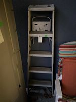 Full view of 5 foot aluminum step ladder against wall showing all steps and top platform with holes.
