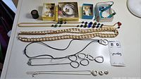 Photo showing assorted necklaces including chain link, pendant styles, bead necklaces; silver and gold tone bangles; and multiple pairs of earrings in small boxes.