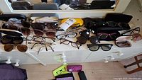 Top view of all sunglasses and eyeglasses laid out on a white dresser with some cases visible