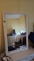 Full view of the rectangular mirror reflecting a room with furniture and books visible.