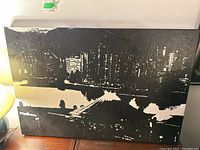 Front view of the black and white cityscape painting on canvas, showing overall composition and texture.