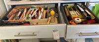 Two kitchen drawers with organized kitchen utensils and cutlery including spoons, forks, scissors, oil brushes, and other small tools.